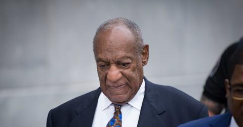 Bill Cosby wears a dark suit, white shirt, and patterned tie.