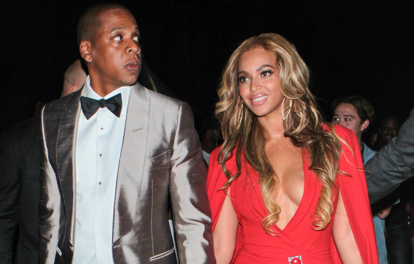 Beyonce wears a red dress with plunging neckline and open sleeves, hair worn long and wavy, alongside Jay Z at a 2015 boxing match.