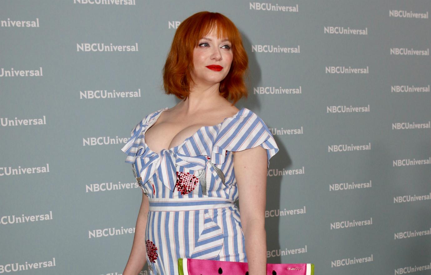 Christina Hendricks wears a cleavage baring striped and floral patterned dress with butterfly sleeves, red hair in a wavy red bob with bangs at the 2018 NBC Upfronts.