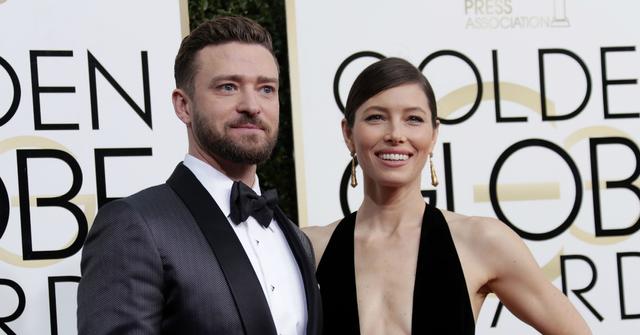 Justin Timberlake, in a black tux and white shirt, stands on the red carpet next to Jessica Biel who wears a black dress with a plunging neckline.
