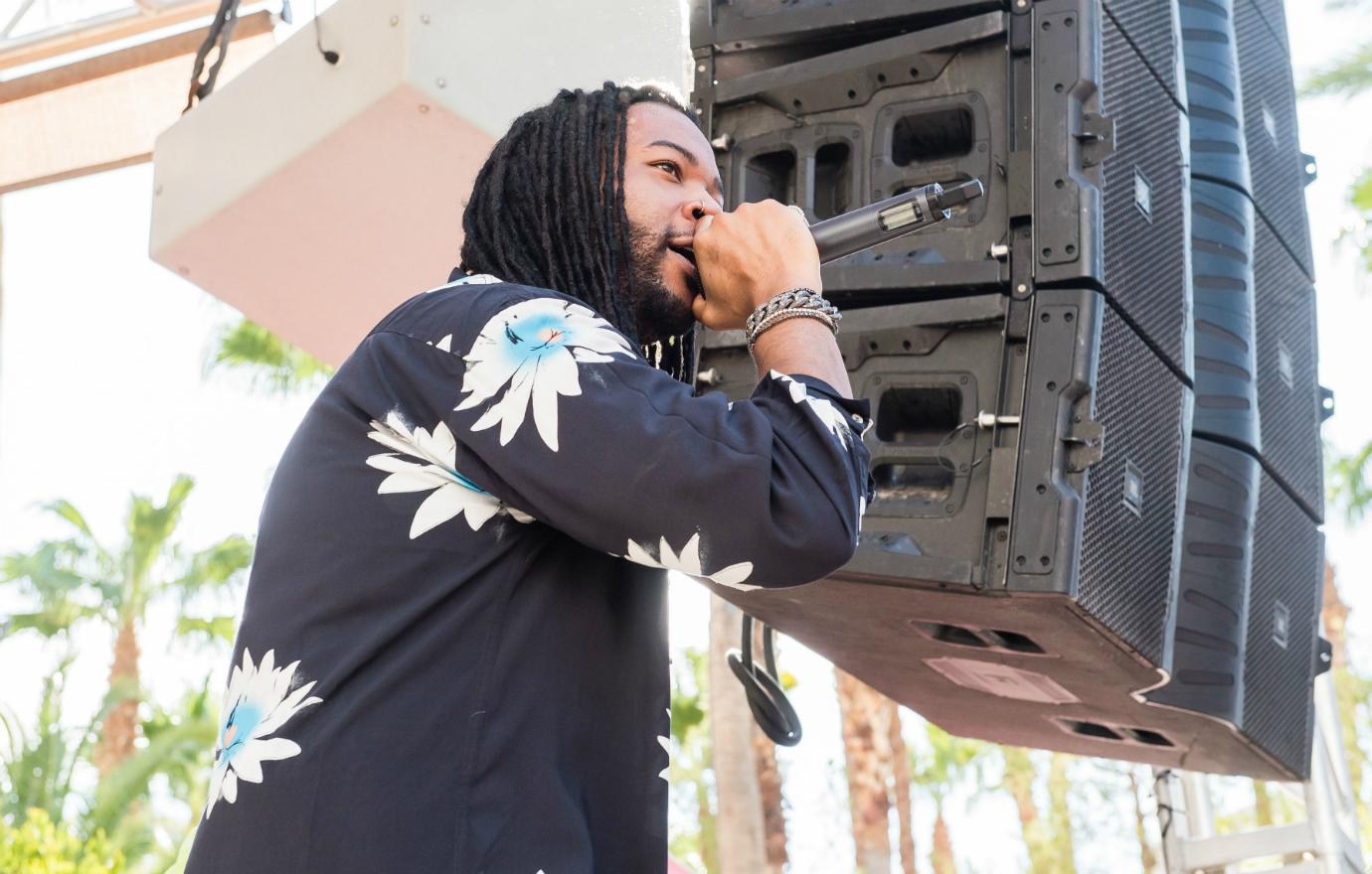 PartyNextDoor performs on stage while wearing a black shirt with white flowers on it.