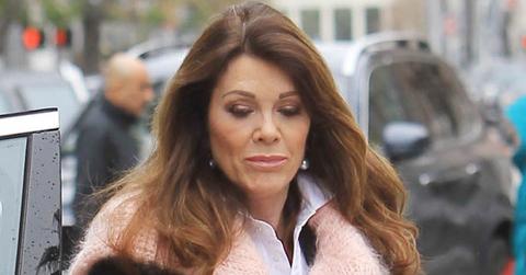 Lisa Vanderpump is seen wearing a pink scarf and a white shirt while looking down.