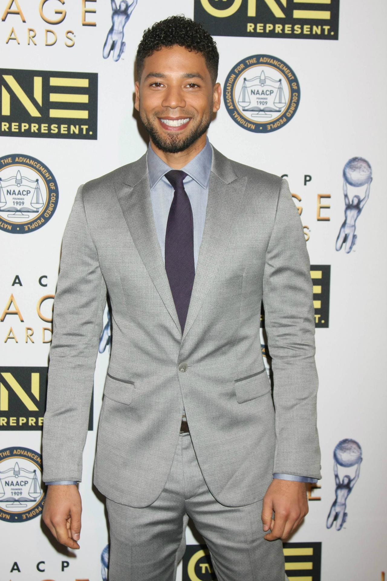 Jussie Smollett wears a gray suit with blue shirt and purple tie.