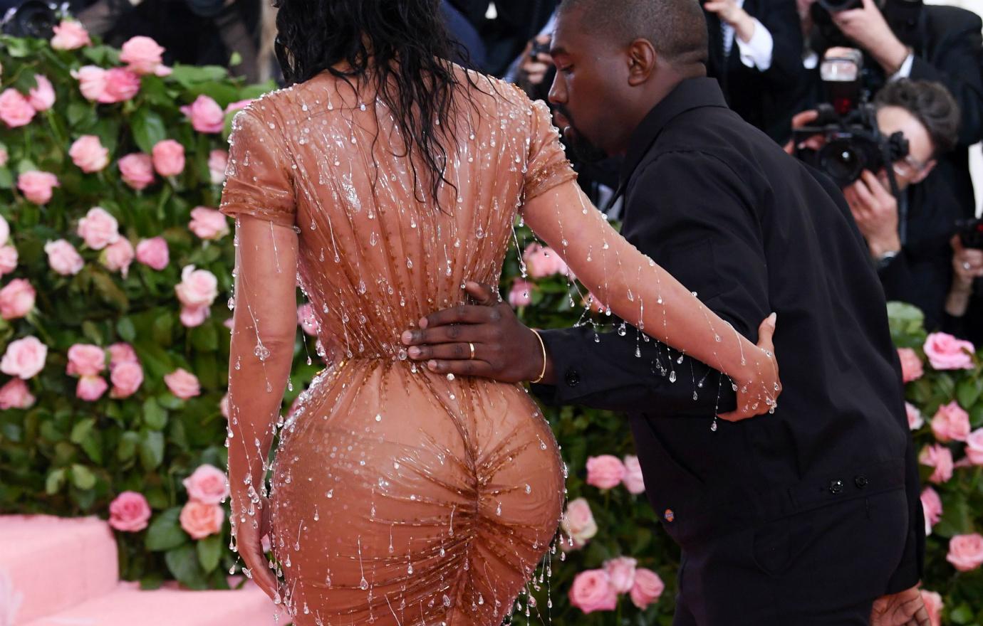 Kim Kardashian, wearing a revealing dress, walks up steps with Kanye West by her side.