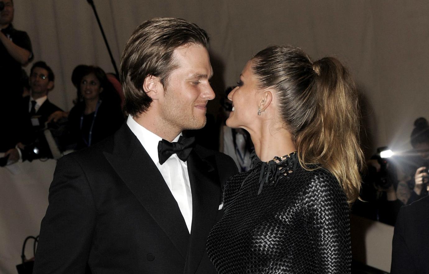 Tom Brady, in a black tux, hugs wife Giselle Bundchen who wears a patterned black dress.