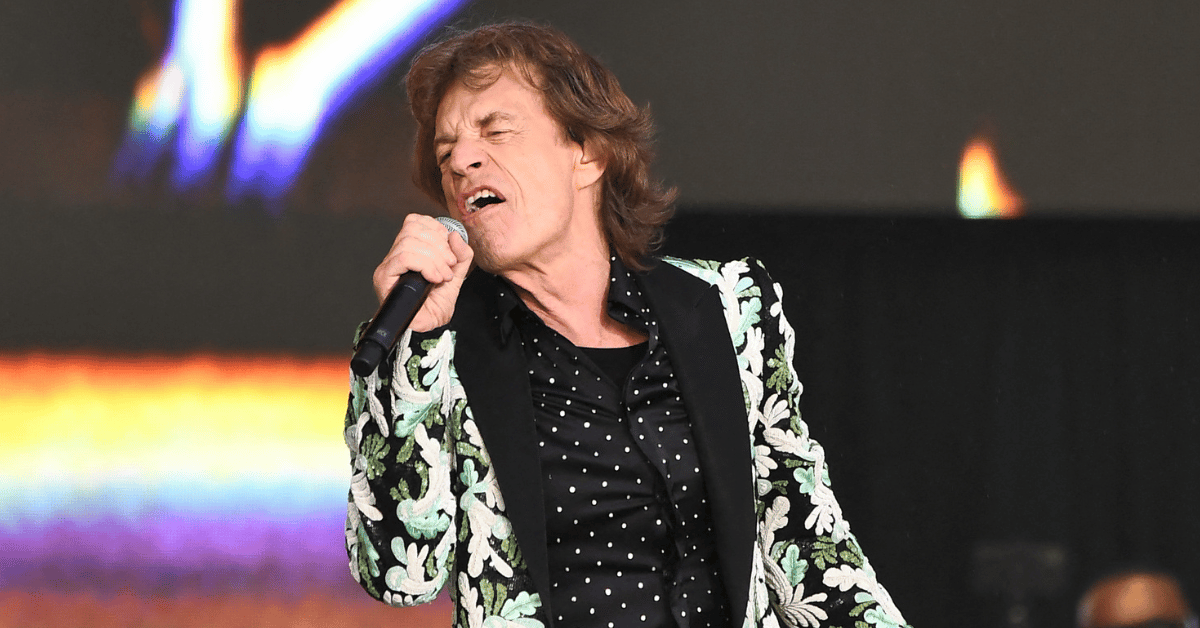 Photo of Mick Jagger performing in green and white suit jacket. 