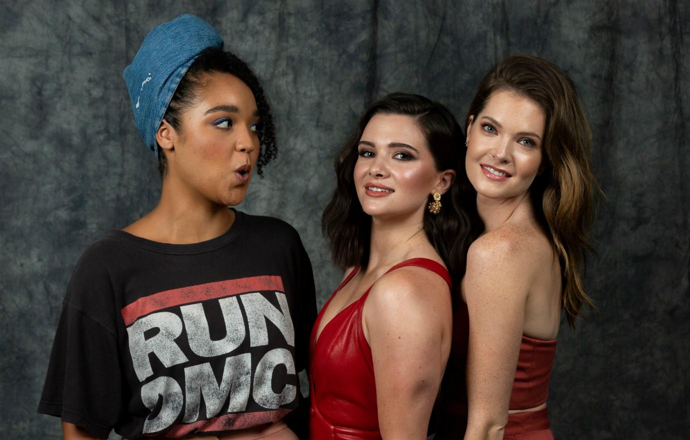 The three main cast members of The Bold Type pose next to each other. Two are wearing red outfits; the third is in a Run DMC tshirt.