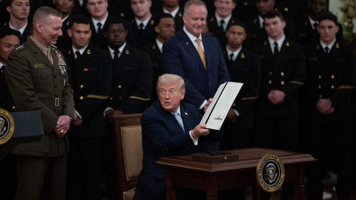 image of The president gripped the desk while easing himself down at the small signing table.