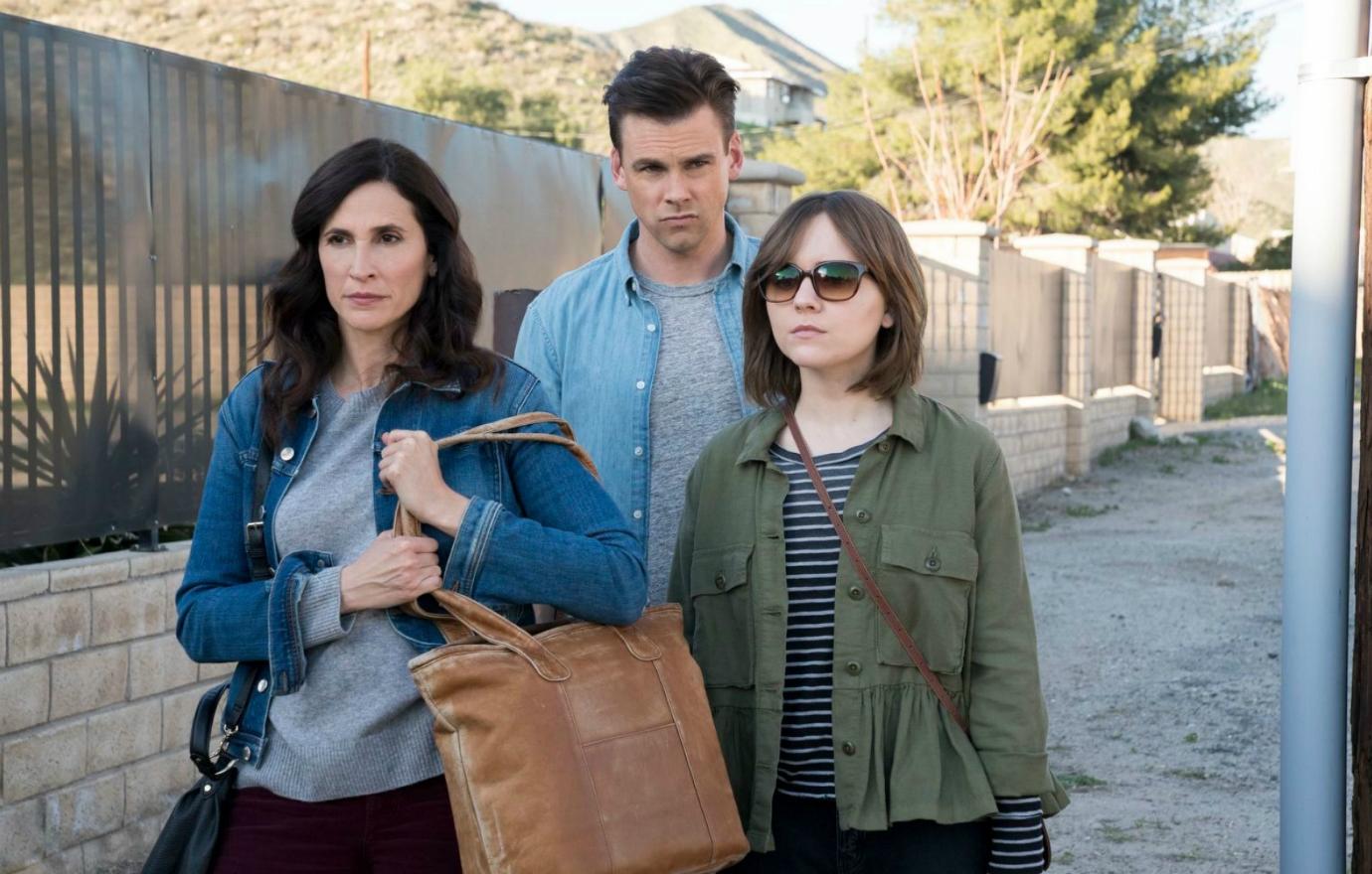 Michaela Watkins in a grey top and blue jacket stands next to Tommy Dewey and Laura Meyers.