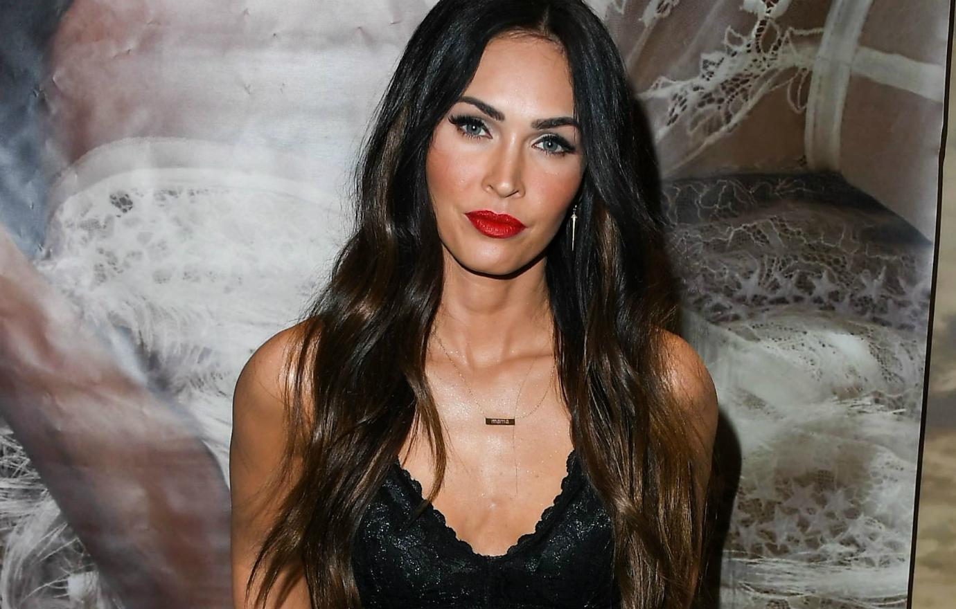 Megan Fox wears a black dress with scalloped neckline, hair long and wavy, and red lip at this 2018 Forever 21 appearance.