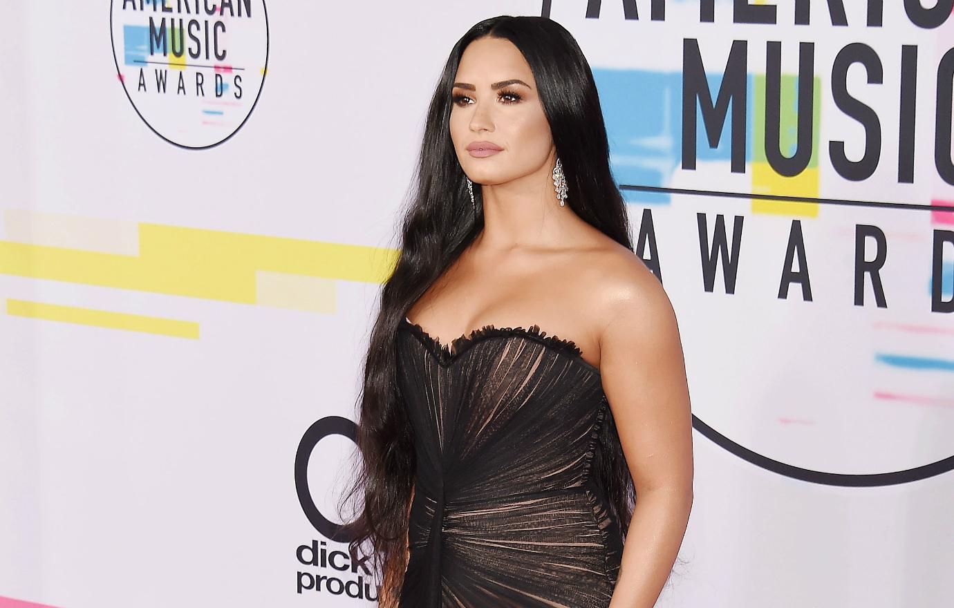Demi Lovato wears a strapless black gown and sparkly earrings, hair long and wavy at the 2017 American Music Awards.