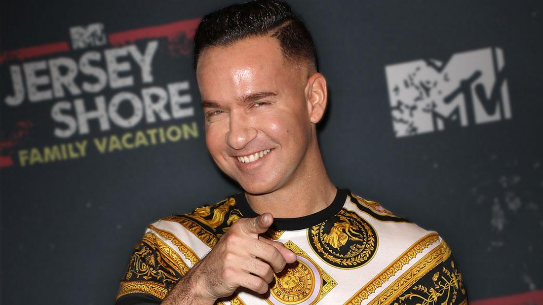 Smiling Mike Sorrentino Pointing At Camera Wearing A Black Gold And White Top