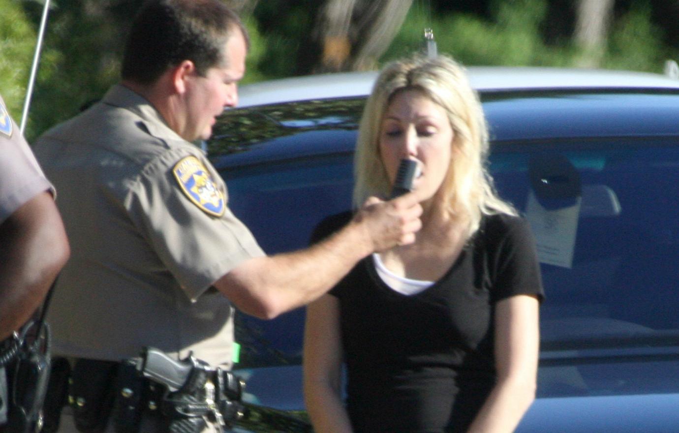 Heather Locklear, in a black top, takes a breathalyzer, administered by a cop.