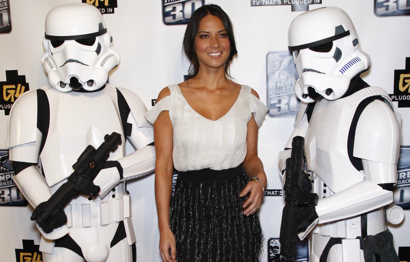 Olivia Munn wears a black mini skirt and white blouse that shows off her shoulders, posing along with storm troopers at 2010 Comic-Con.