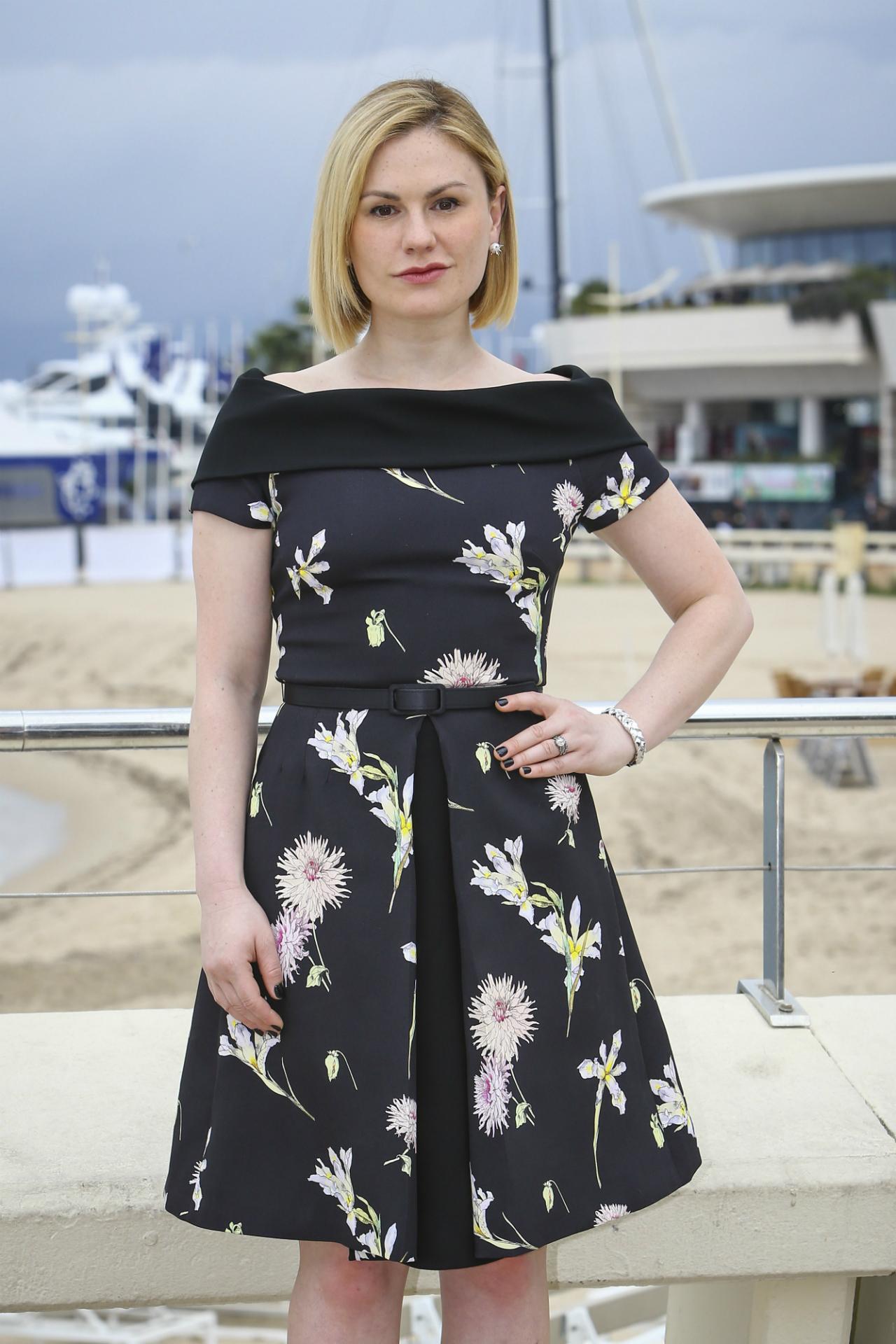 Anna Paquin wears a black floral off the shoulder knee length dress with a slim black belt, blonde bob hairstyle.