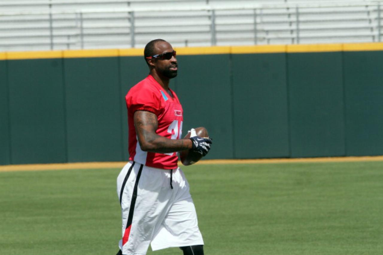 Brandon Browner holds a football as he walks across a field.