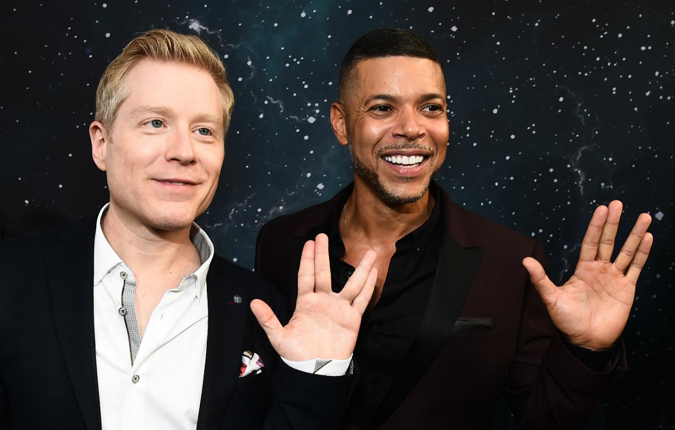 Wilson Cruz, in a black suit and Anthony Rapp in black jacket and white shirt both display a ‘live long and prosper’ hand signal on the red carpet.