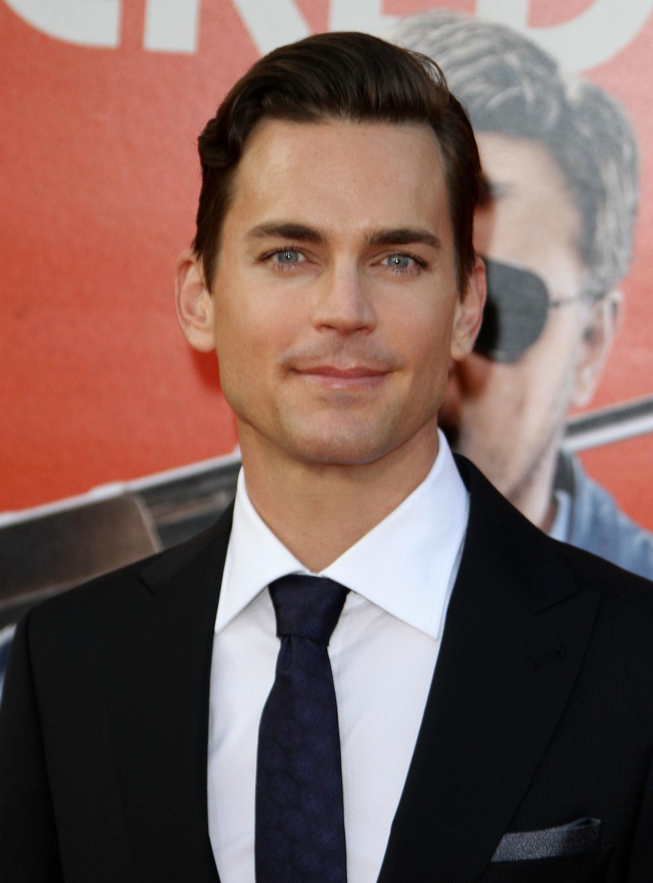 Matt Bomer wears a black jacket, white shirt, and navy blue tie.