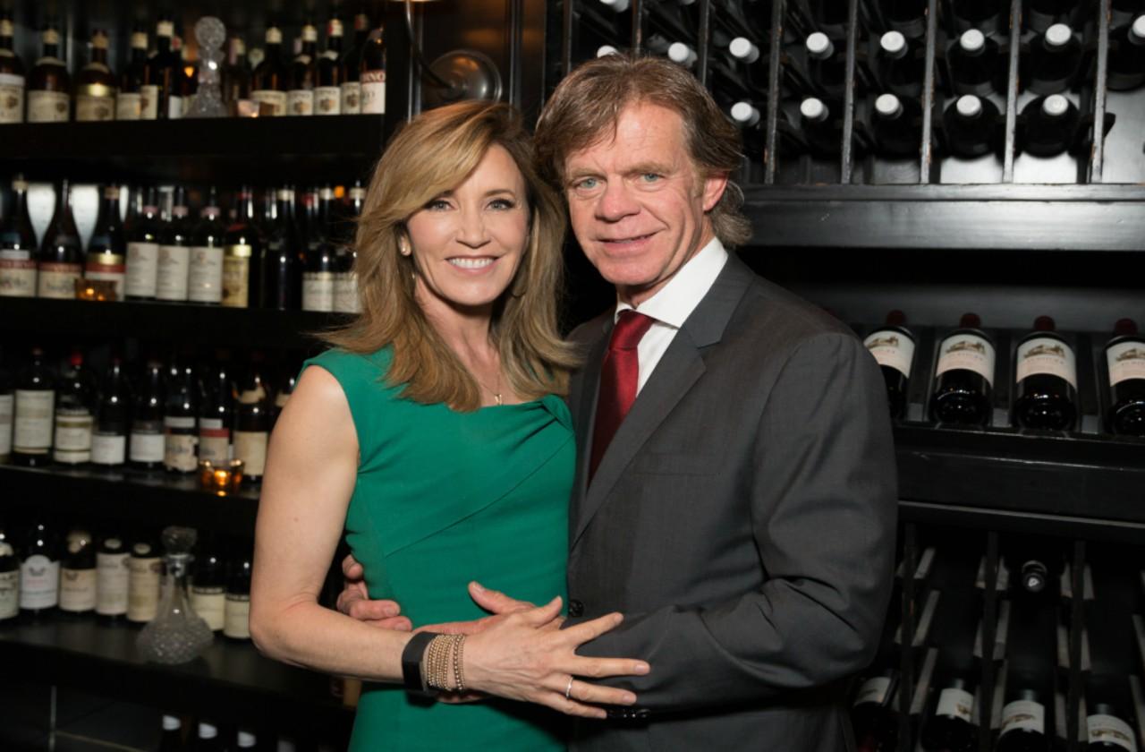 Felicity Huffman in a green dress with William H Macy in a black suit, in front of a wall of wine bottles