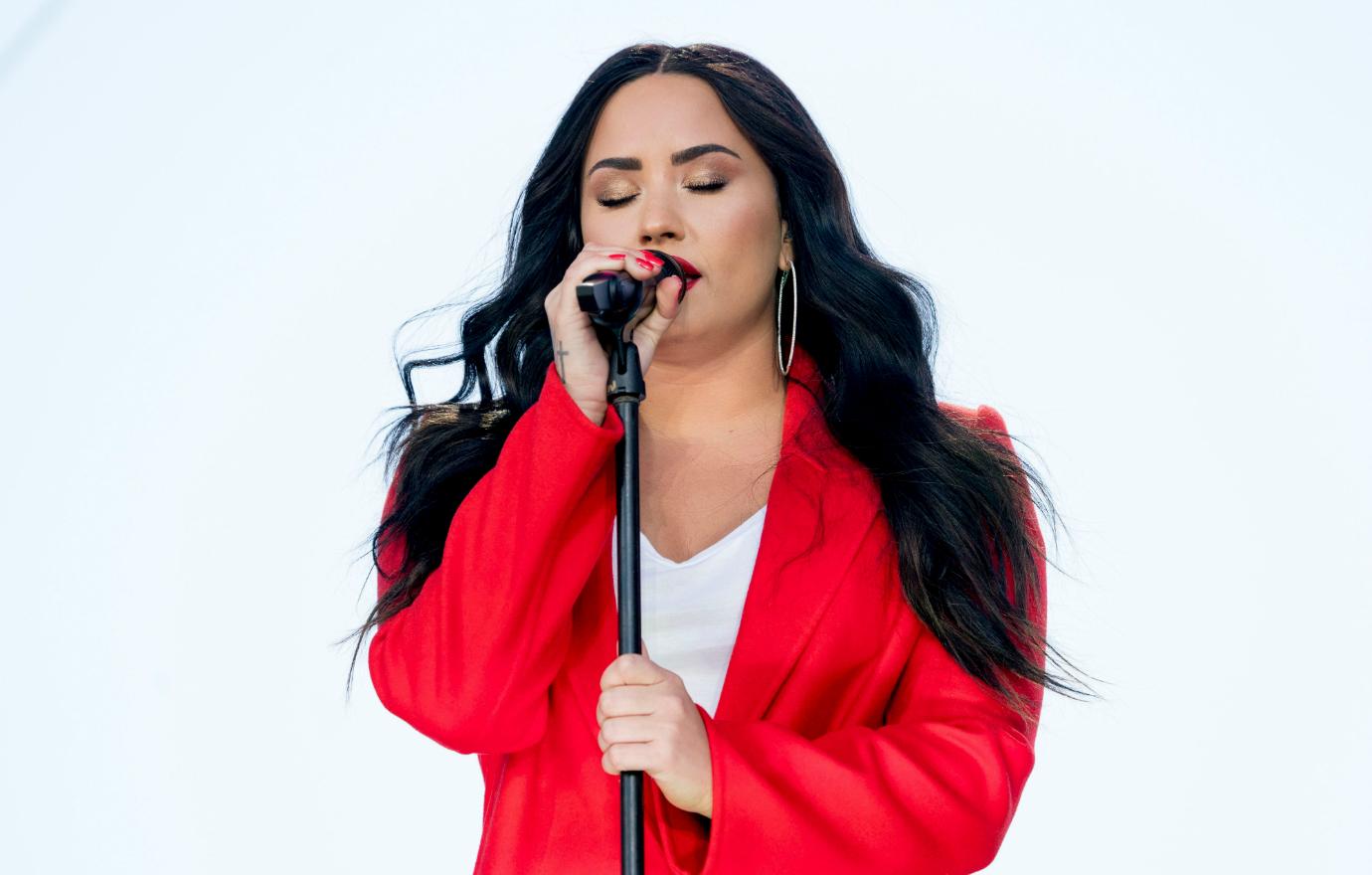 Demi Lovato performed at a women’s march in a red overcoat and a white v-neck T-shirt.