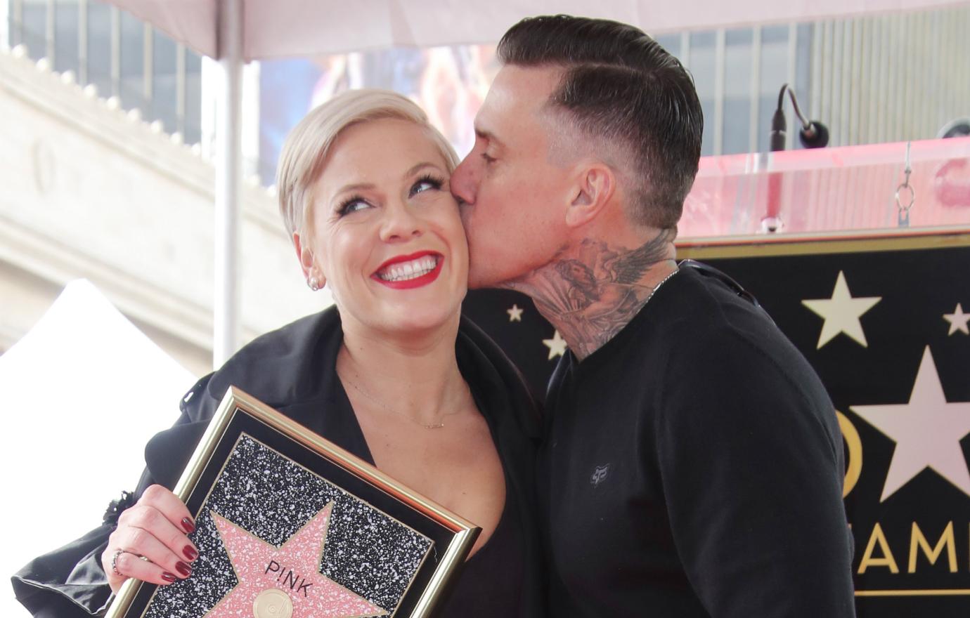 Pink, in a black and white dress, clutches a walk of fame picture and is being kissed by Carey Hart.