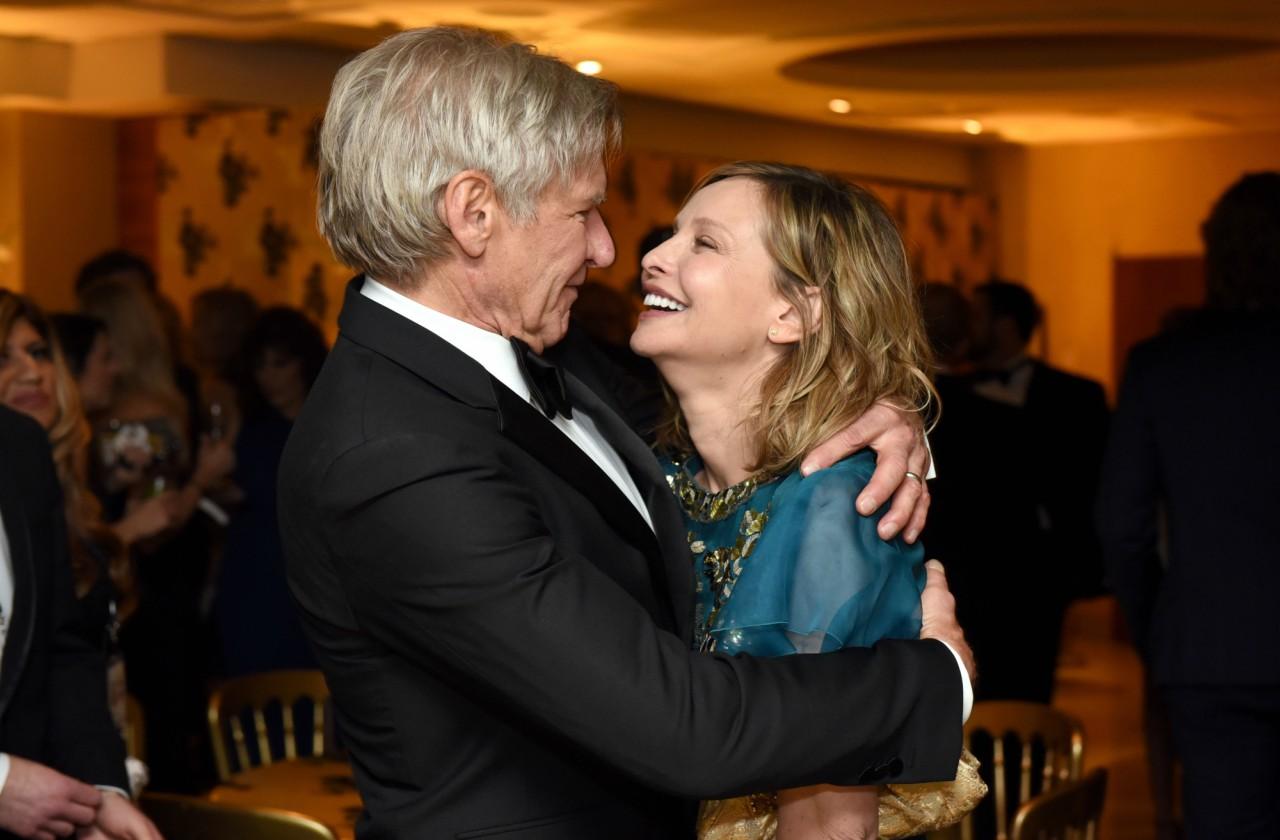 Harrison Ford in a black suit, embraces Calista Flockhart in a teal dress