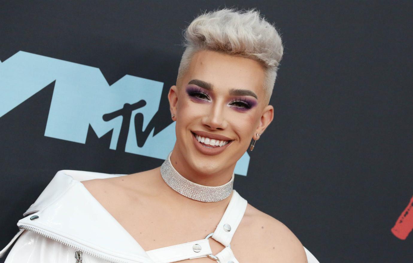 James Charles wears a white top and choker and smiles from the red carpet.