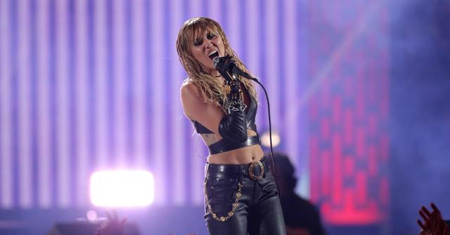 Miley Cyrus clad in black performs on stage.