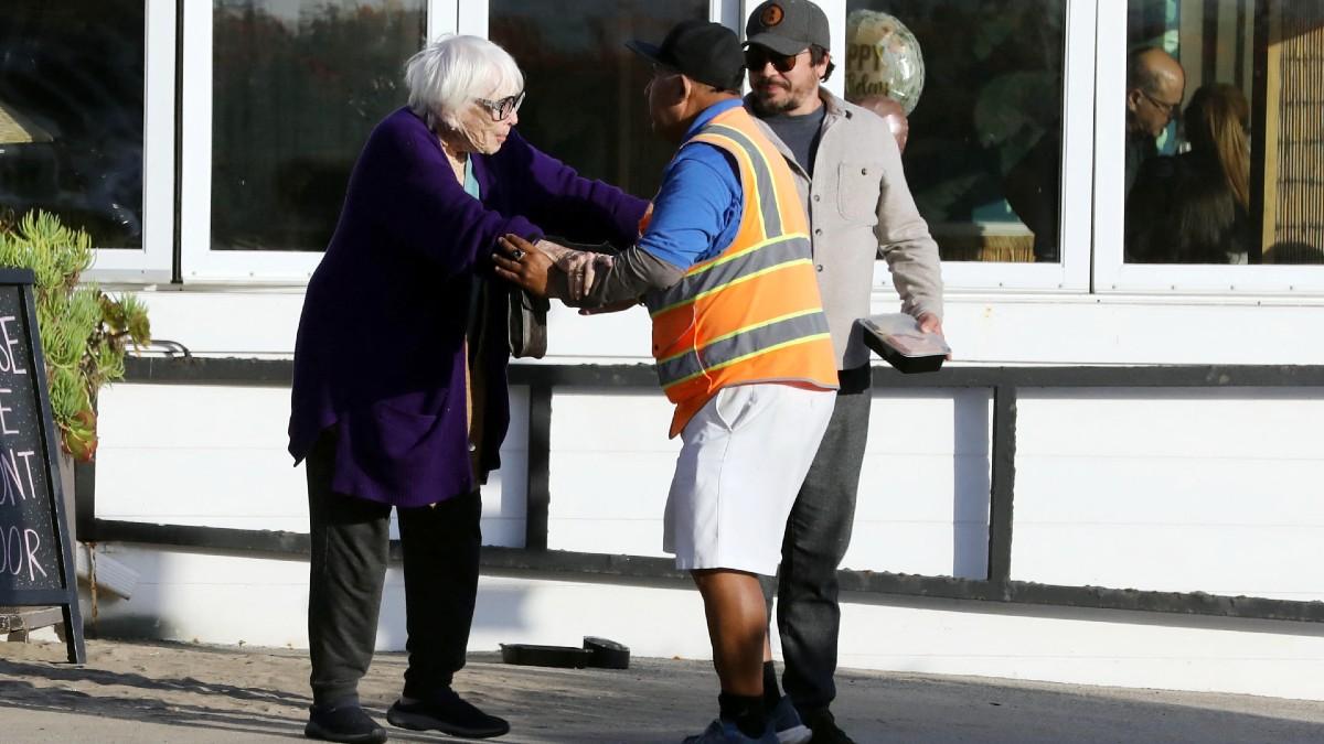 image of MacLaine's companion carried leftovers while helping guide her safely to a nearby vehicle.