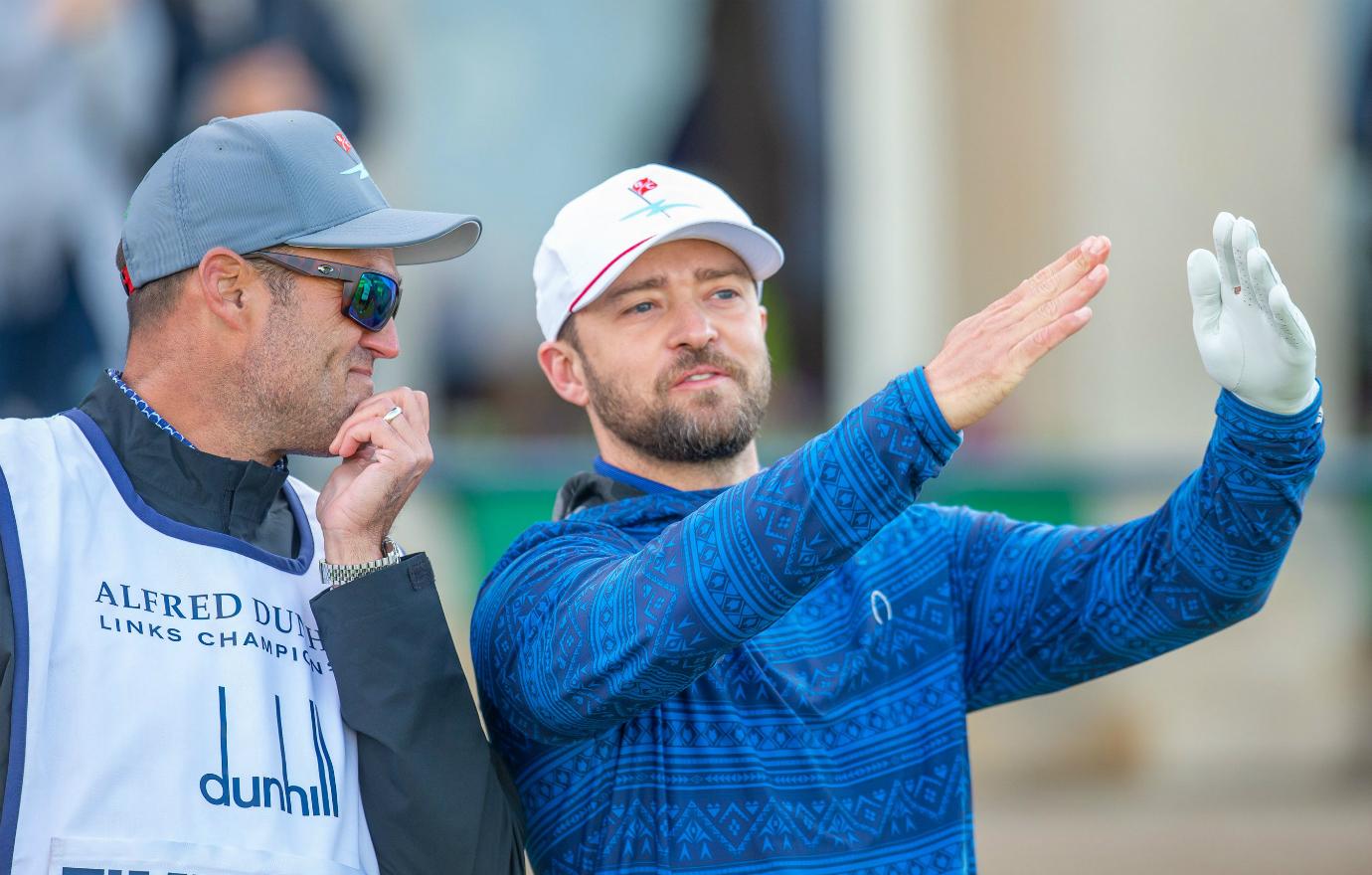 Justin Timberlake, in blue patterned top and white cap talks to his caddy.