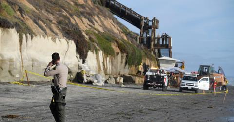 A San Diego County Sheriff's deputy looks on as search and rescue personnel work at the site of a cliff collapse at a popular beach, in Encinitas, Calif.