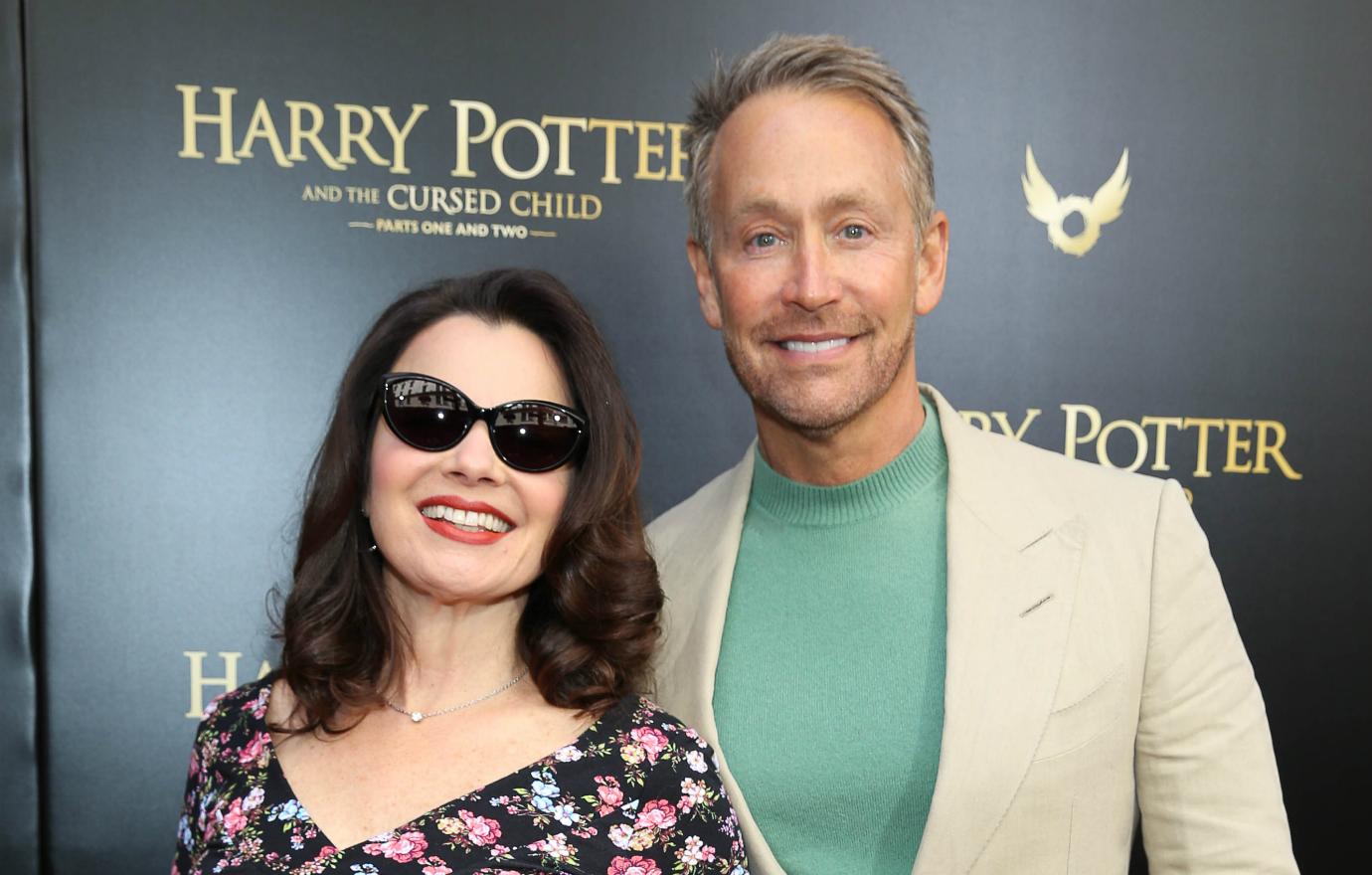 Fran Drescher, in a flowered dress, stands next to Peter Marc Jacobson who wears a tan jacket and pants and light green sweater.