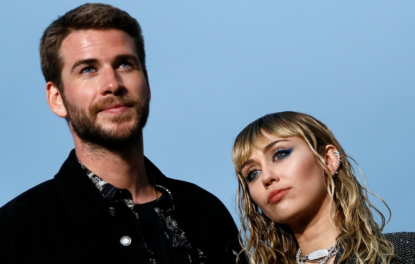 Liam Hemsworth stands next to Miley Cyrus as the pose on the beach.