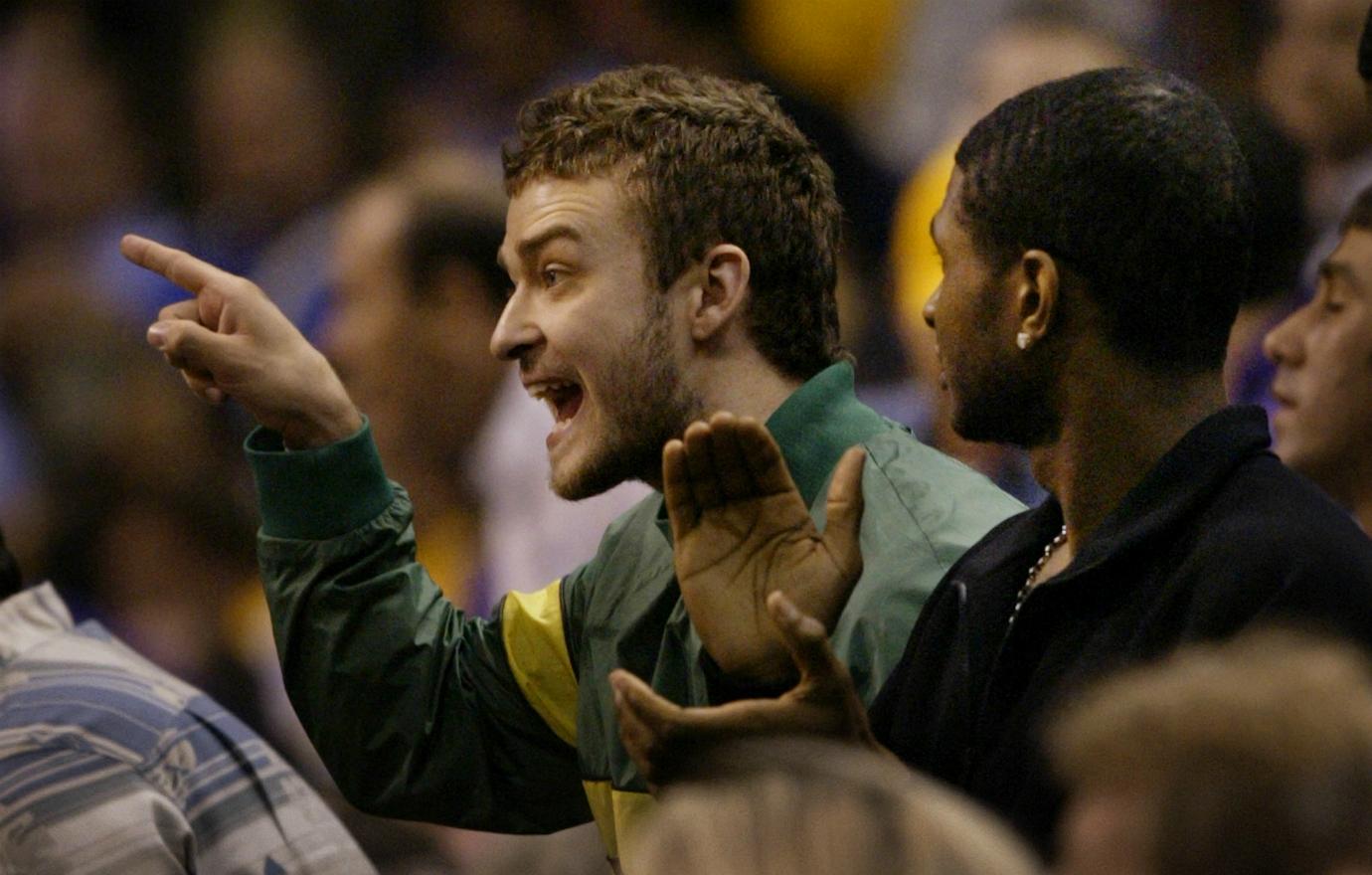 Justin Timberlake, in a green jacket, points animatedly at the court as Usher stands next to him, clapping.