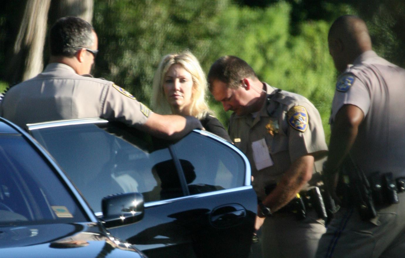 Heather Locklear, in a black top, is cuffed by police as she stands by her car.