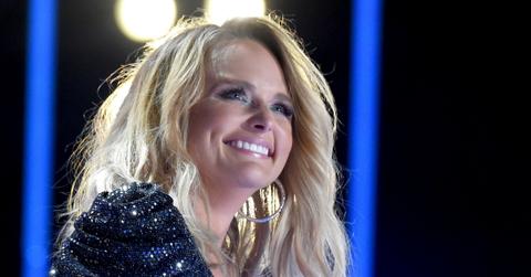 Miranda Lambert smiles while on stage, wearing a sparkly black dress.