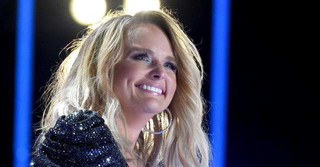 Miranda Lambert smiles while on stage, wearing a sparkly black dress.