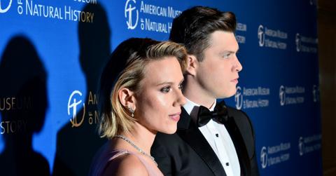 Colin Jost, in a black tux, stands next to Scarlett Johansson who wears a pink dress on the red carpet.