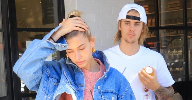 Justin Bieber wears a white shirt and a white cap. Hailey Baldwin is in front with a denim jacket and a pink sweater.