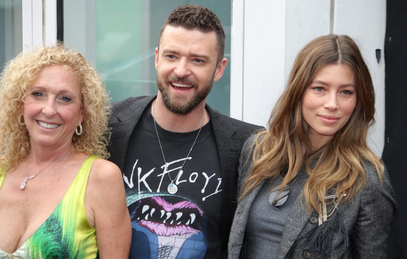 Lynn Harless, in a patterned yellow dress, stands next to Justin Timberlake who wears a Pink Floyd t-shirt and black jacket and Jessica Biel who wears a black top and black jacket.