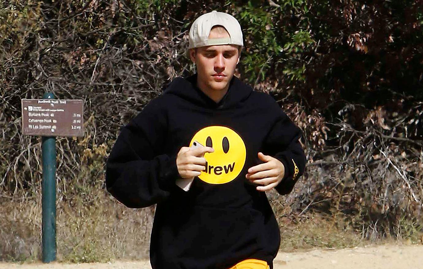 Justin Bieber jogs in white baseball cap and black top with a smiley face on it.