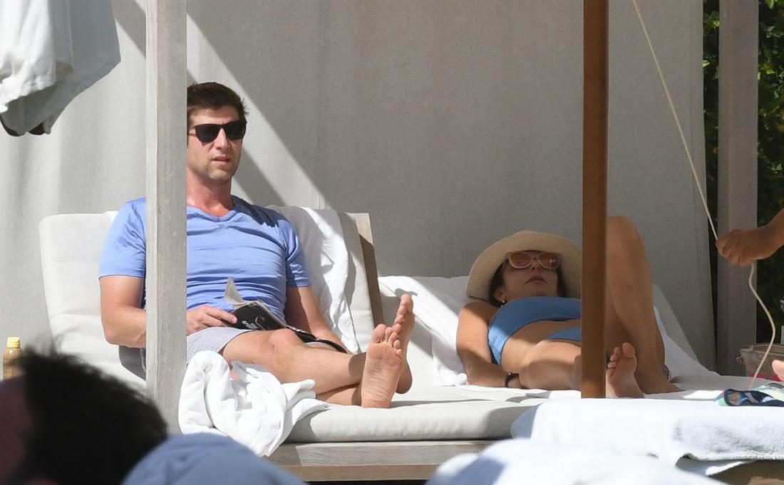 Paul Bernon, in a blue t-shirt, lays on a lounger next to Bethenny Frankel who wears a matching blue swimsuit.