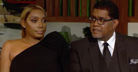 Nene Leakes Wearing One Shoulder Black Dress Sitting With Husband Greg Leakes Wearing A Brown Three Piece Siut White Shirt, Brown Tie