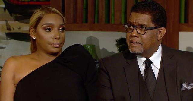 Nene Leakes Wearing One Shoulder Black Dress Sitting With Husband Greg Leakes Wearing A Brown Three Piece Siut White Shirt, Brown Tie
