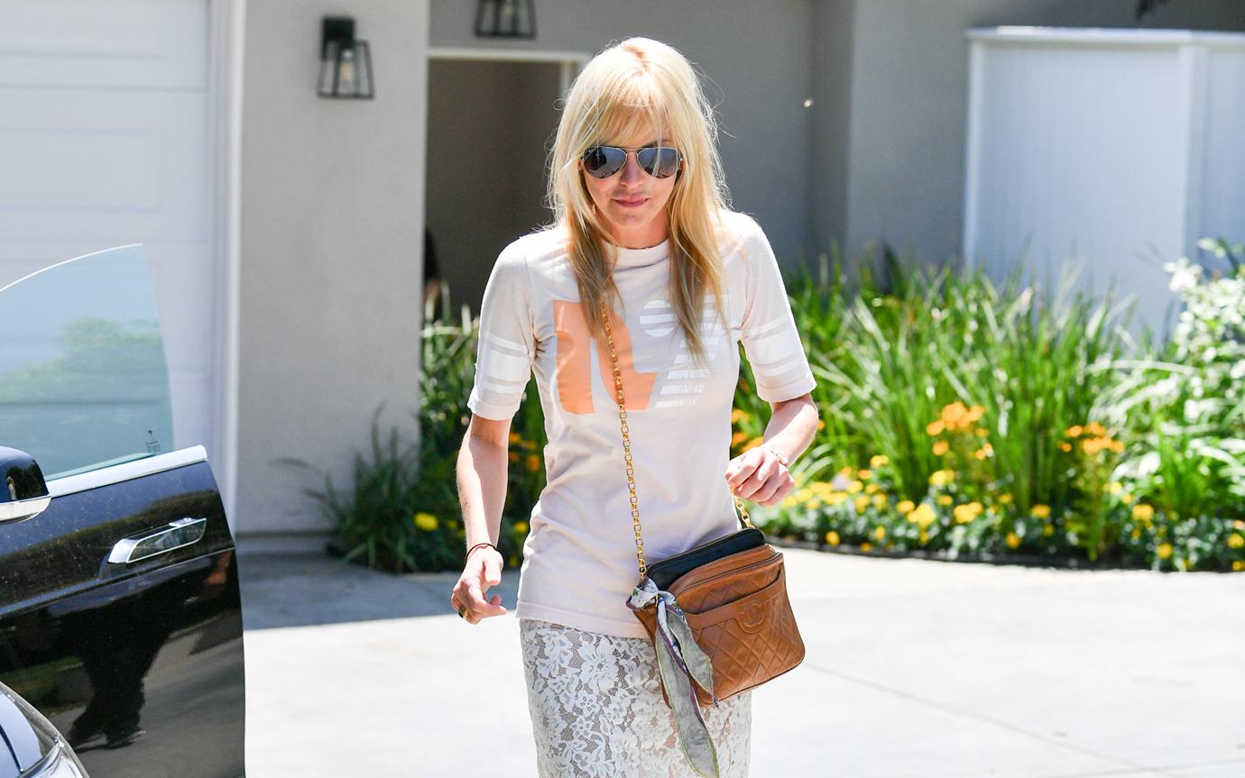 Anna Faris wears a white top and skirt while walking towards her car.