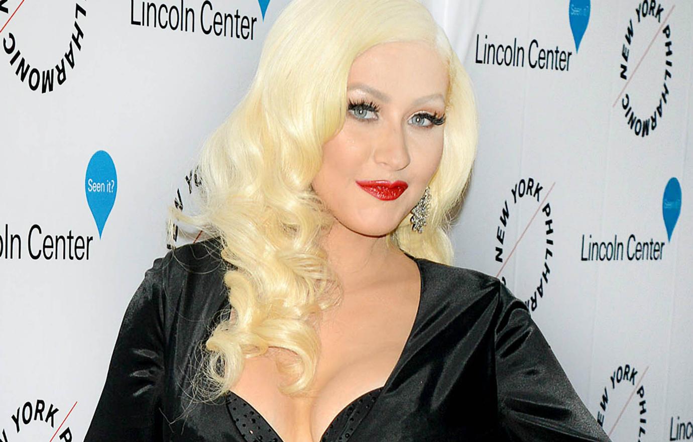 Christina Aguilera wears a low cut black dress with red lip and platinum blonde hair in loose curls at this 2015 Lincoln Center event.