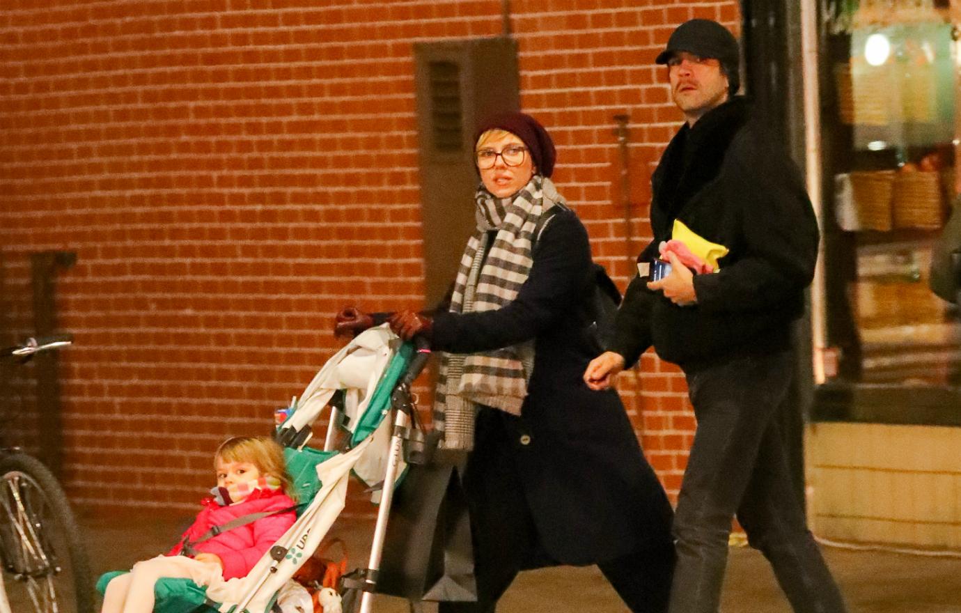 Scarjo, in a black coat and striped scarf, pushes her baby in a stroller.