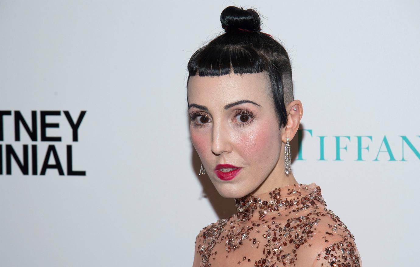 Michelle Harper, her hair tied into a small bun, stands on the red carpet in an orange patterned dress.