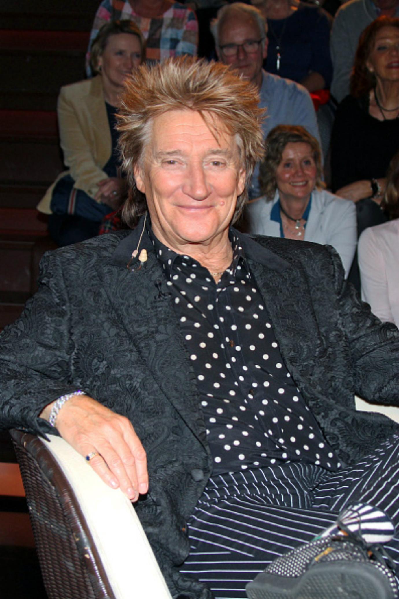 Rod Stewart smiles while sitting in a chair.