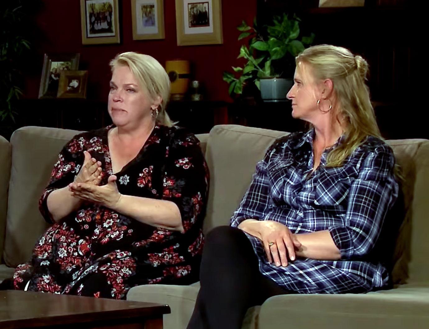 Brown Wives, Janelle Wearing Red an Black Flowered Dress With ChristineWearing Blue and Black Plaid Top Sitting on Couch